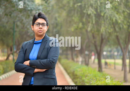 Closeup portrait of a confident young Indian Corporate professional woman with short hair and spectacles, crossed folded hands in an outdoor