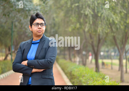 Closeup portrait of a confident young Indian Corporate professional woman with short hair and spectacles, crossed folded hands in an outdoor setting Stock Photo