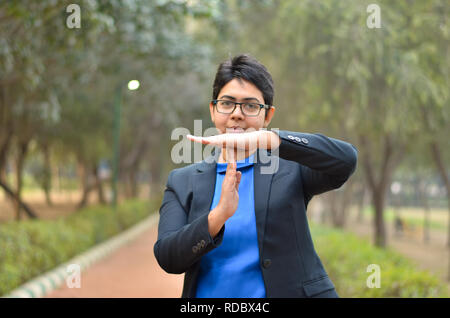 Portrait of confident young Indian Corporate professional woman with short hair showing timeout sign in outdoor setting wearing a black business suit Stock Photo