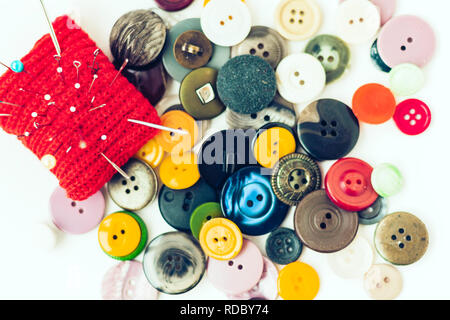 Red knitted needle pad for sewing, sewing buttons and colored thread coils on white background Stock Photo