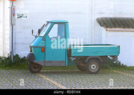 parked up mini Italian truck or pickup called an ape which means bee in English with three wheels in a car park by a wall near the sea in Italy Stock Photo