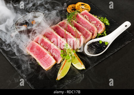 Sliced tuna steak with lime and sesame in puffs of white smoke. Stock Photo