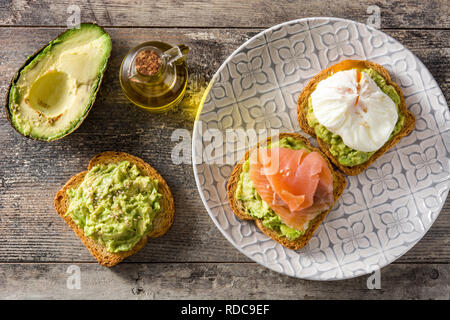 Toasted breads with poached eggs, avocado and salmon in plate on wooden table. Top view. Stock Photo
