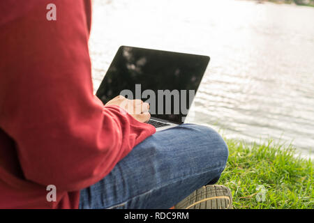 Man hands typing on laptop next to the lake Stock Photo