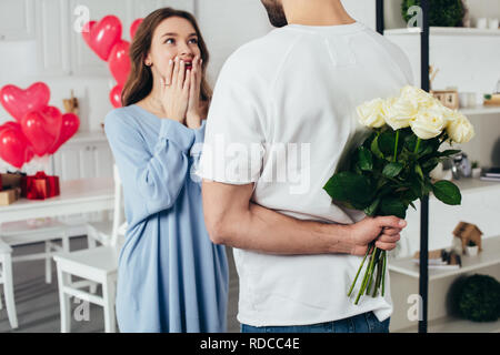 partial view of a young man holding bouquet of flowers behind back while smiling girlfriend waiting for surprise Stock Photo