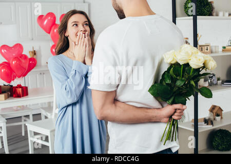 partial view of a young man holding bouquet of roses behind back while smiling girlfriend waiting for surprise Stock Photo