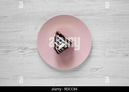 Piece of homemade chocolate cherry cake on a pink plate over white wooden background, overhead view. Flat lay, from above, top view. Stock Photo