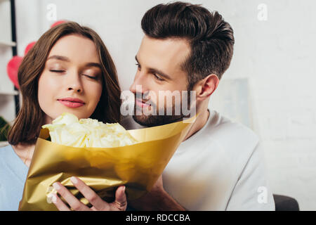 smiling girl with closed eyes smelling roses bouquet near boyfriend Stock Photo