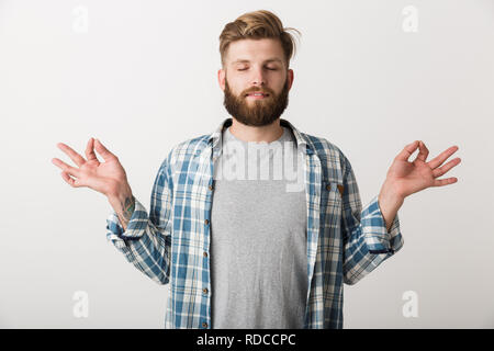 Calm young man dressed in plaid shirt standing isolated over white background, meditating with eyes closed Stock Photo