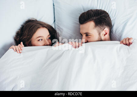 young loving couple hiding under blanket in bed and looking into eyes Stock Photo