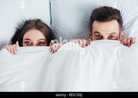 adult couple hiding under blanket in bed Stock Photo