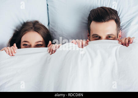 woman and man smiling and hiding under blanket in bed Stock Photo