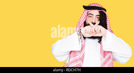 Arabian business man with long hair wearing traditional keffiyeh scarf Rejection expression crossing fingers doing negative sign Stock Photo