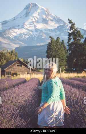 Portrait of Blonde adult woman stands in a lavender field, smiling, in the golden hour before sunset Stock Photo
