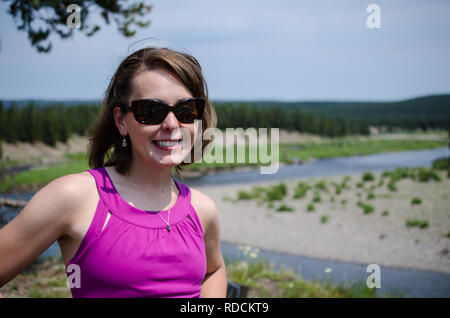 Portrait of a young woman tourist posing at an overlook in Yellowstone National Park. Woman is wearing sunglasses and smiling Stock Photo