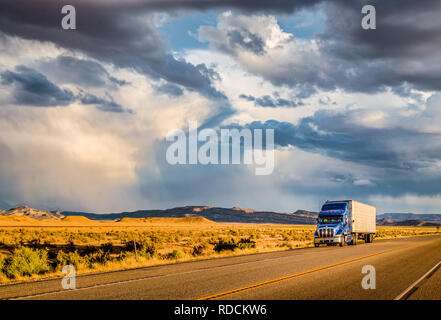 Beautiful panorama view of classic semi trailer truck on empty highway with dramatic sky in golden evening light at sunset Stock Photo