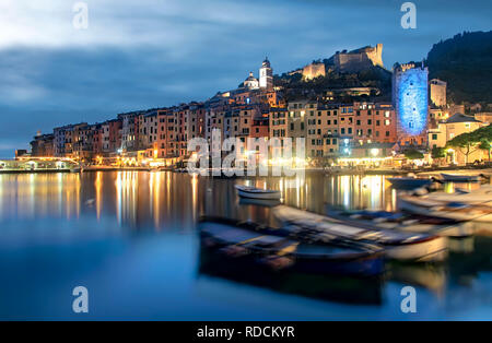 Twilight over Portovenere with colorful reflections from illuminated waterfront buildings and foreground fishing boats in a tourism and travel concept Stock Photo