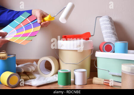 Painting tools for home on parquet with white wall background and painter choosing colors on a color chart. Horizontal composition. Front view. Stock Photo