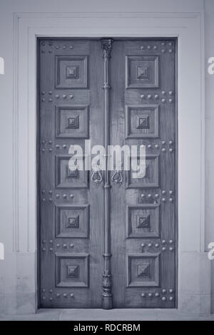 Wooden old catholic church door. Converted black and white. Toned blue. Stock Photo