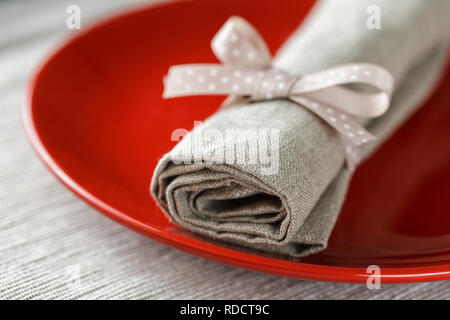 Red plate with grey linen napkin tighten with ribbon. Festive table set, dining textiles Stock Photo