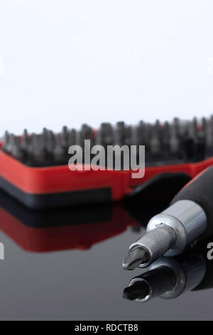 Screwdriver with phillips head with various bits in a case in the background reflected on a glass surface Stock Photo