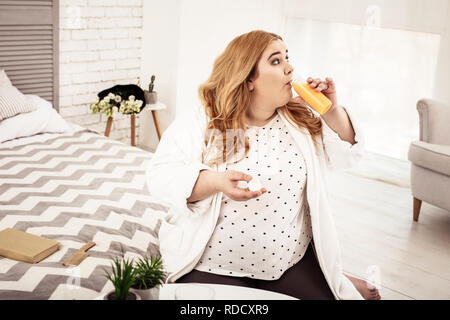 Big overweight young woman drinking freshly-made orange juice Stock Photo