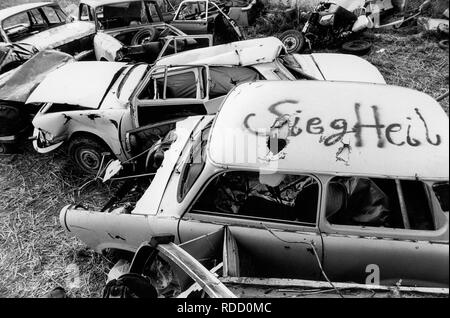 GERMANY in 1990 after reunification, former East Germany, German Democratic Republic GDR, typical plastic car Trabant also called Trabbi with fascist Nazi Hitler greeting Sieg Heil and Wartburg car on wild dumping site in village Plauerhagen, Mecklenburg, people have dumped their East German car in exchange to new western cars, scan from black and white negative with film grain