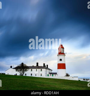 A wet & windy winter sunrise, a brief glimse of the sun lights up the clouds before dark storm clouds quickly follow engulfing the lighthouse Stock Photo