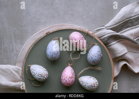 Top view of decorative handmade Easter eggs in pastel colors on wooden tray with linen towel Stock Photo