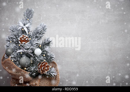 Small Christmas tree in sackcloth decorated with red baubles and berries on light stone background with copy-space Stock Photo