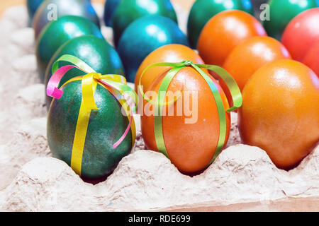 Brightly colored bow decorated easter eggs in egg carton holder, holiday background Stock Photo