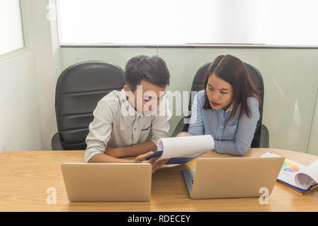 Serious conversation between two Asian business employees at work Stock Photo
