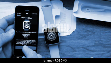 PARIS, FRANCE - APR 12 2018: POV man unboxing unpacking latest Apple Watch Series 3 GPS LTE smartwatch during the shared sync procedure enabling - blue color cast  Stock Photo