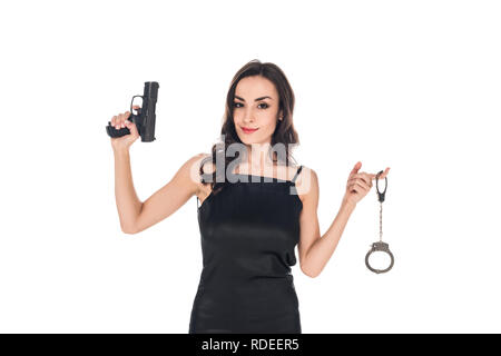 attractive smiling secret agent in black dress holding gun and handcuffs, isolated on white Stock Photo