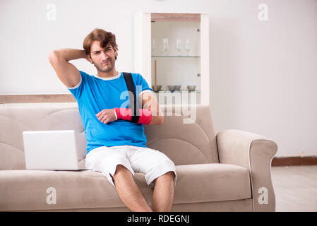 Young man with injured arm sitting on the sofa Stock Photo