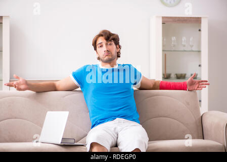Young man with injured arm sitting on the sofa Stock Photo