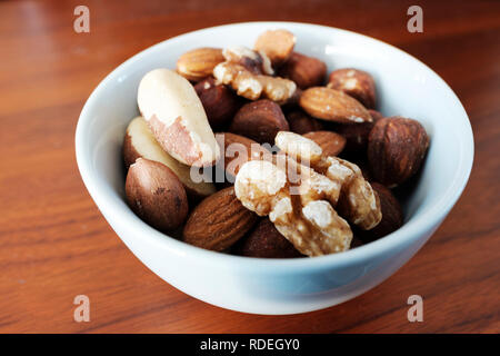A small white bowl that is full with different types of nuts Stock Photo