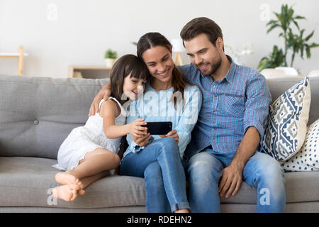 Smiling mother holding smartphone taking family selfie or watchi Stock Photo