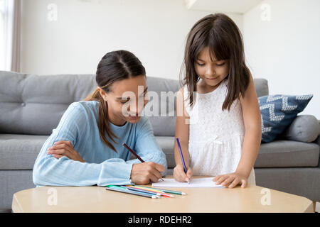 Focused mom holding colored pencil teaching kid daughter to draw Stock ...