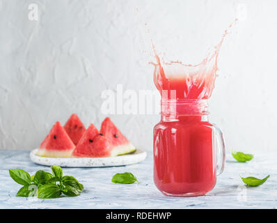 Tasty appetizing watermelon drink with basil in mason jar on gray table. Homemade watermelon and basil lemonade with splashes. Copy space. Slice water Stock Photo
