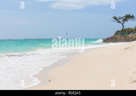 A white beach at Silver Sands, Barbados. Ocean waves roll in. Kitesurfers play in the safe waters off-shore. Stock Photo
