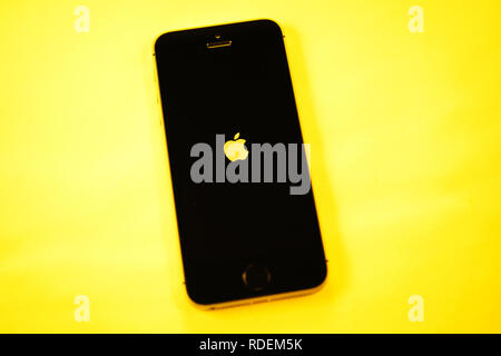 Paris, France - Apr 21, 2016: Newest Apple Computers iPhone SE smartphone after unboxing on yellow background with Apple logotype on the digital retina display Stock Photo