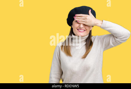 Middle age mature woman wearing winter sweater and beret over isolated background smiling and laughing with hand on face covering eyes for surprise. B Stock Photo