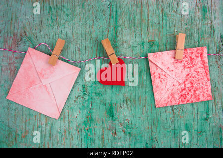 vintage  red paper envelops and paper red heart hung on clothespins on a rope on a mint green wall background Stock Photo