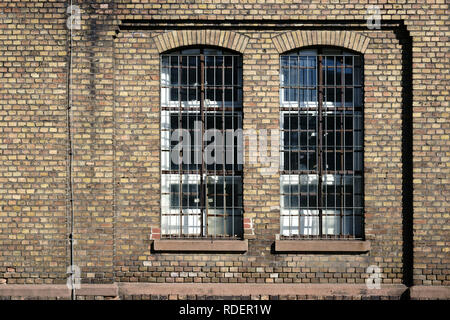 A brick wall on the disused industrial site of an old factory with a barred window. Stock Photo