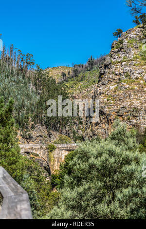 View of mountains and a old roman bridge over Paiva river, in stone, with vegetation around, in Arouca, Portugal Stock Photo