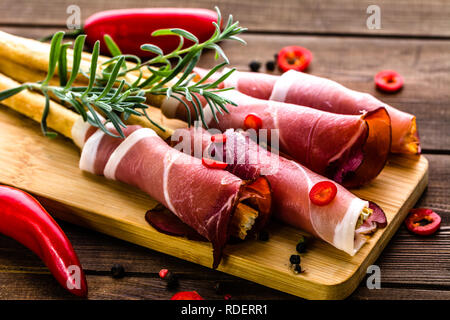 Sticks of bread with prosciutto, italian antipasto, food platter with meat, cold appetizer on wooden table Stock Photo