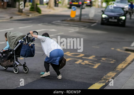 LONDON, UK – May 14, 2018: Woman with child in dangerous situation in crossing busy street. Stock Photo