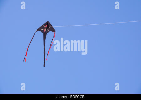 angle view of a colorful kite flying with waving red bow in a deep blue sky with the light of the sun Stock Photo