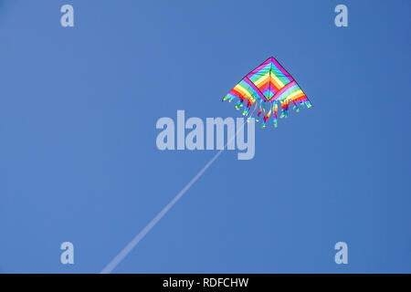 angle view of a colorful kite flying with waving red bow in a deep blue sky with the light of the sun Stock Photo